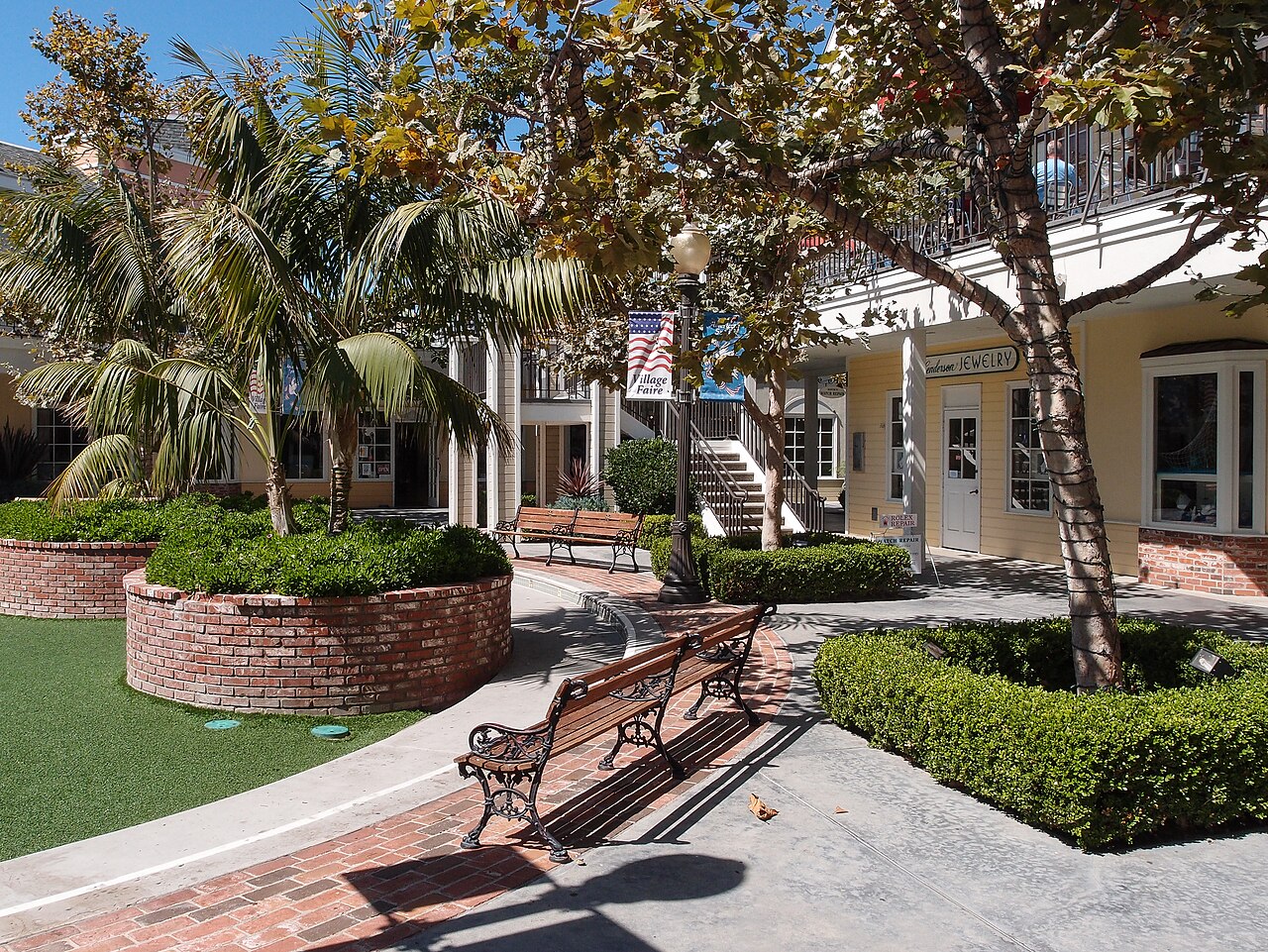 The Village Faire courtyard with palm trees, brick planters, garden benches, and two-story shops